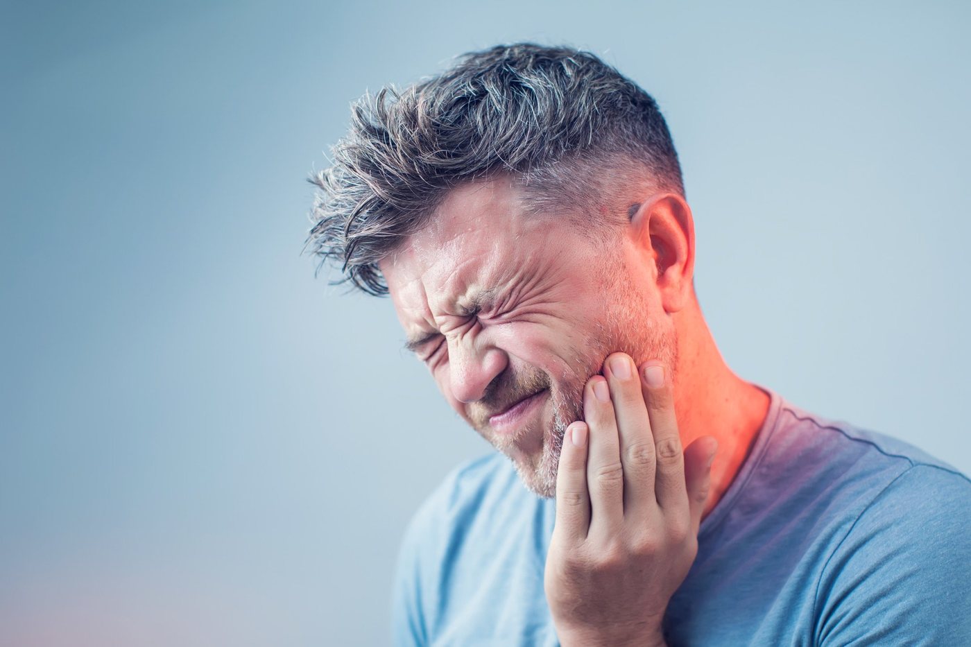 A man holding his jaw, wincing from tooth pain